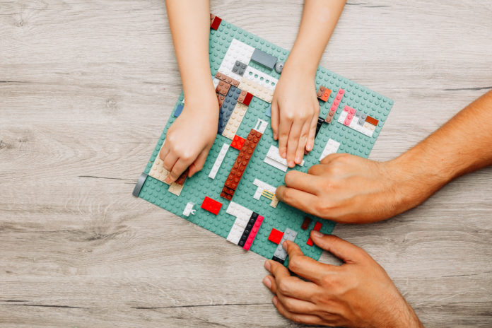 Father and daughter playing with legos on light wooden background, top view.